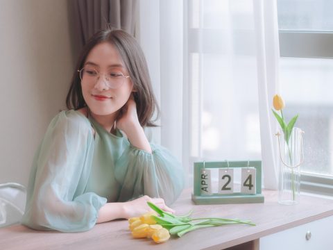 玩家坐在窗前用平板查看米游社签到与福利页面，窗外是傍晚的城市灯火